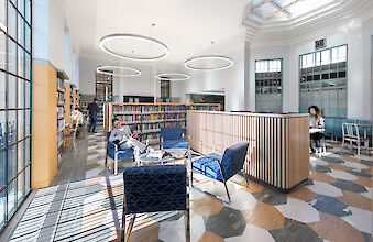Large library room with ring pendant lights, reading places, bookshelves and geometrically patterned floor