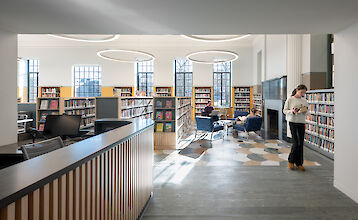 Bright library with high windows, reading corner, bookshelves and modern reception desk