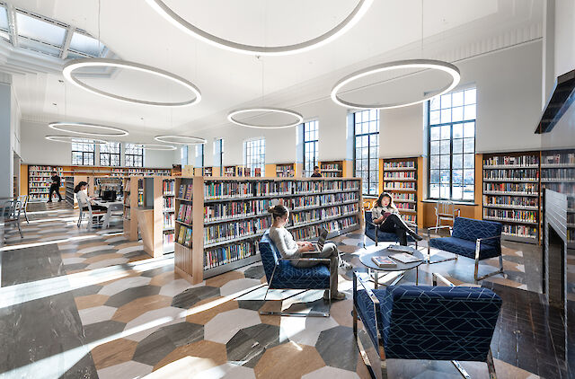 Bright library with ring pendant lights, bookshelves, reading area and geometric floor pattern