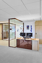 Modern office with glass walls, double monitor workstation and linear pendant lighting system above the desk.