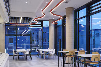 Interior de un moderno restaurante de empresa con luminarias Liquid Line curvadas y ventanas que van del suelo al techo.
