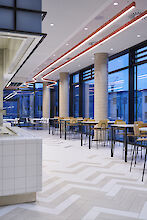 Vista de un restaurante para el personal con mesas altas, columnas de hormigón visto y luminarias lineales Liquid Line