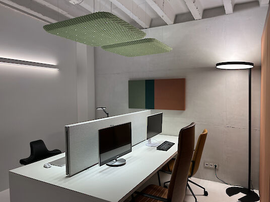 Moderner Büroarbeitsplatz mit Serenity-Akustikleuchten, Trennwand, Monitoren und Stehleuchte vor Sichtbetonwand.