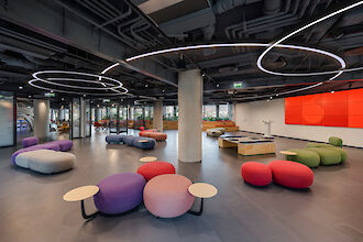 Spacious open space with colourful seating islands, dark ceiling and sculptural ring lights from Lightnet
