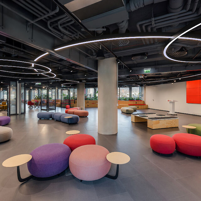 Spacious open space with colourful seating islands, dark ceiling and sculptural ring lights from Lightnet