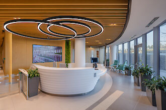 Bright reception area with round counter, large ring pendant lights and floor-to-ceiling windows with natural light
