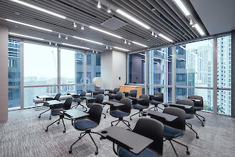 Bright seminar room with individual tables, modern chairs, and floor-to-ceiling windows with city views