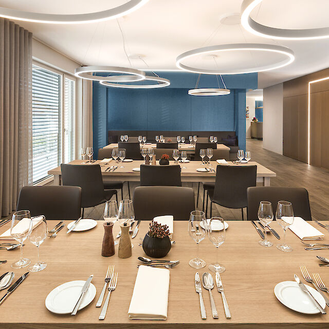 Eleganter Meeting- und Essbereich mit gedeckten Tischen und großen runden Pendelleuchten von Lightnet