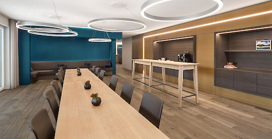 Modern meeting area with long wooden table, blue seating alcove and large round pendant lights