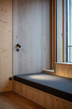 Niche revêtue de bois avec banquette et rembourrage gris au Håndværkskollegiet ; un spot Midpoint noir de Lightnet éclaire le coin salon près de la fenêtre
