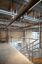 Vue intérieure d'un escalier dans le Håndværkskollegiet avec poutres apparentes, structures métalliques et deux spots Midpoint noirs de Lightnet au plafond.