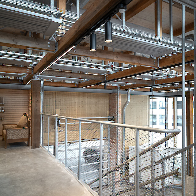 Innenansicht eines Treppenbereichs im Håndværkskollegiet mit sichtbaren Holzträgern, Metallkonstruktionen und zwei schwarzen Midpoint-Strahlern von Lightnet an der Decke