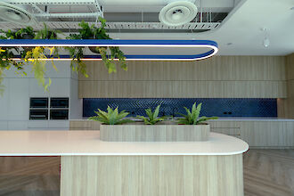 Lámpara colgante Liquid Line azul sobre isla de cocina con plantas, frentes de madera y panel trasero de azulejos azules