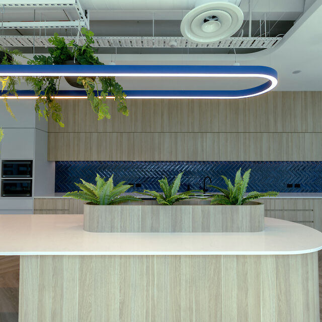 Lámpara colgante Liquid Line azul sobre isla de cocina con plantas, frentes de madera y panel trasero de azulejos azules