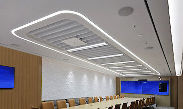 Moderna sala de conferencias con una gran mesa, sillones de cuero, revestimiento de madera y luces lineales integradas en el techo
