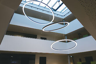 Drei ringförmige Ringo Star LED-Pendelleuchten von Lightnet im lichtdurchfluteten Atrium des Rathauses Delbrück