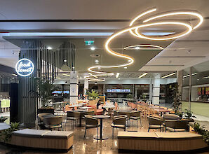 Modern food court with round seating islands and curved Liquid Line LED ceiling lights