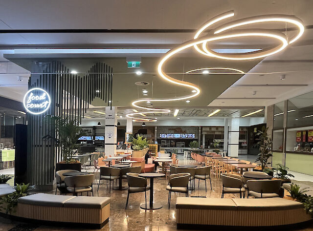 Modern food court with round seating islands and curved Liquid Line LED ceiling lights