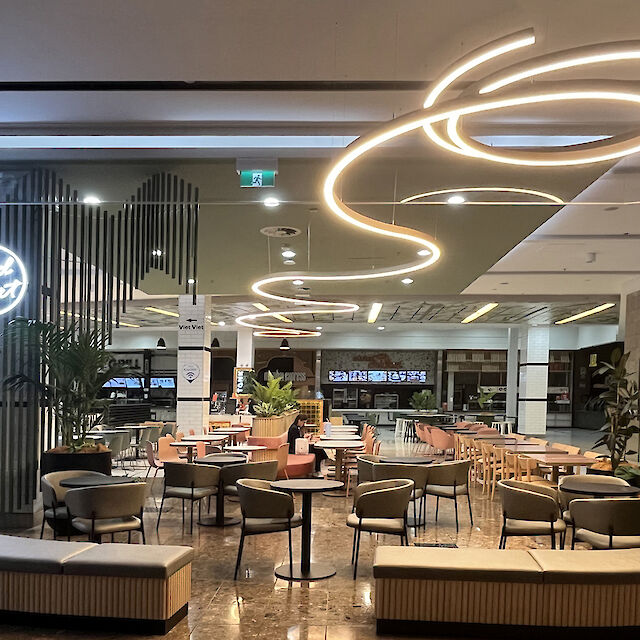 Modern gestalteter Foodcourt mit runden Sitzinseln und geschwungener Liquid Line LED-Deckenleuchte