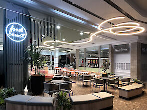 Elegant food court with modern seating areas, plants, and curved Liquid Line LED ceiling lights.