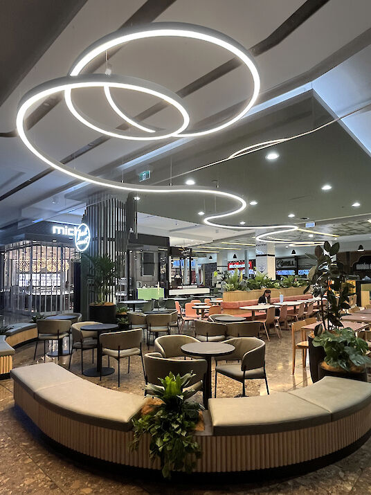 Modern lounge with round seating islands, plants, and curved Liquid Line LED ceiling lights.