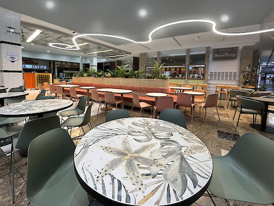Modern café with patterned tables, colorful chairs, and curved Liquid Line LED ceiling lights.