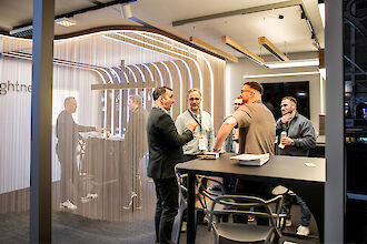 Mehrere Messebesucher im Gespräch am Lightnet-Stand, umgeben von Kettenvorhang und modernen Leuchten.