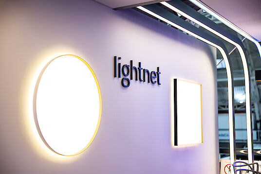 Hochwertig beleuchteter Lightnet-Messestand mit runden und eckigen Leuchten sowie modernen Linienstrukturen