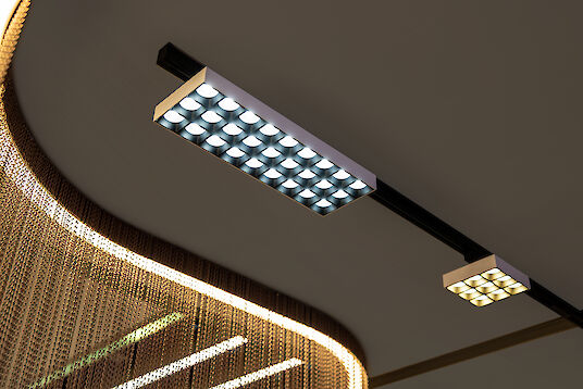 Rechteckige und quadratische LED-Module in Schienenmontage, vor beleuchtetem Kettenvorhang sichtbar