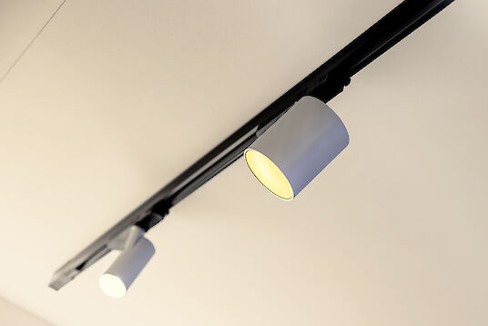 Zwei zylindrische LED-Strahler in schwarzer Schiene, warm leuchtend gegen helle Decke montiert.