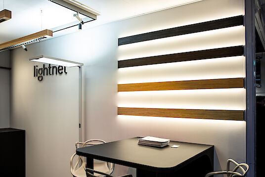 Beleuchtete Matric-Leuchten mit Holzverkleidung an der Wand, daneben Tisch und Stühle im Lightnet-Stand