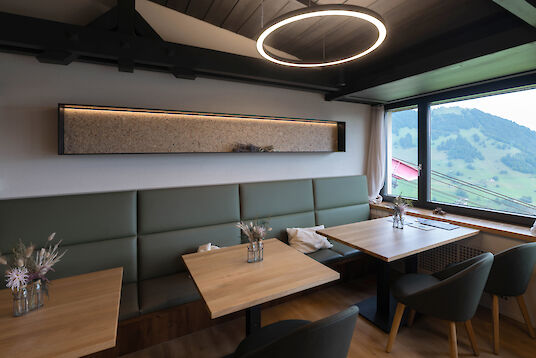 Modern restaurant interior with round Ringo Star pendant light, wooden tables, upholstered benches and alpine views