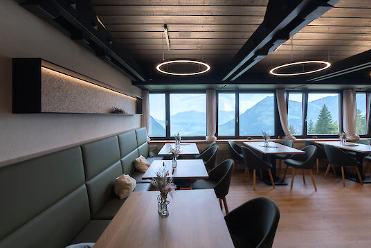 Intérieur du restaurant avec plusieurs suspensions rondes Ringo Star, tables en bois, banquettes rembourrées et vue panoramique sur les montagnes