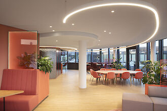 Espace de bureau ouvert avec tables rondes, plantes et lignes lumineuses Liquid Line incurvées au plafond