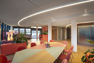 Grand espace de réunion avec mobilier coloré, plantes et lignes lumineuses Liquid Line incurvées au plafond