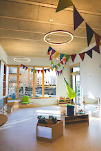 Heller Spielraum mit bunten Wimpeln, Hängesessel, Spielzeug, großen Fenstern und Deckenleuchten