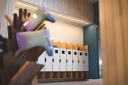 Garderobenbereich mit Holzlamellen, Schließfächern und linearer Deckenleuchte Matric, ruhig und funktional.