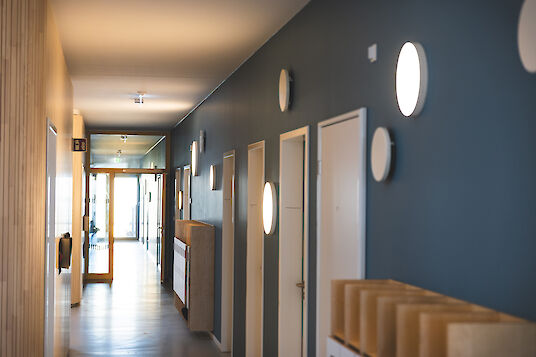 Langer Flur mit Holzoberflächen, blauer Wand und runden Wandleuchten Basic, gleichmäßig beleuchtet