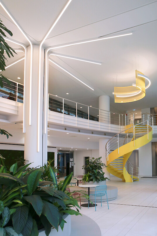 Atrium mit verzweigten Liquid Line Lichtlinien, gelber Treppe und Pflanzeninseln