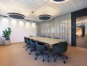 Konferenzraum mit großem Tisch, Vorhängen und ringförmigen Deckenleuchten