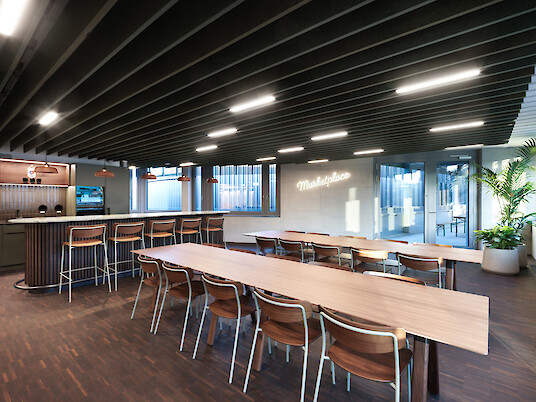 Grande salle commune avec de longues tables en bois et des luminaires linéaires Matric au plafond