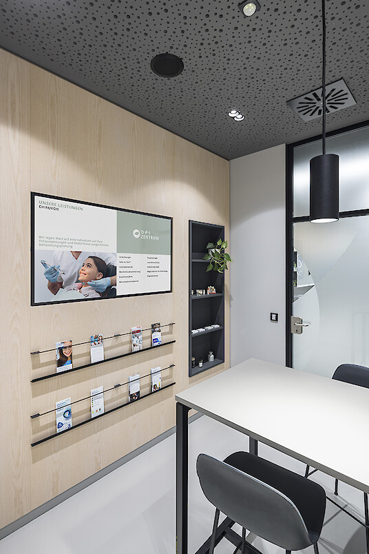 Beratungsraum mit Midpoint Pendelleuchte, Holzwand, Informationsdisplay und perforierter Decke