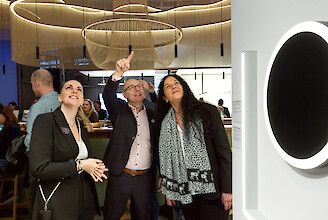 Drei Personen betrachten Lichtinstallation, zeigen nach oben, stehen in Messeumgebung mit Leuchten