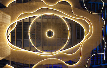 Leuchtinstallation mit konzentrischen Kreisen, radialen Linien und organisch geschwungenen Lichtformen in warmem Licht