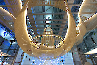 Große Lichtinstallation mit ringförmigen Leuchten und herabhängenden, filigranen Ketten in warmem Licht