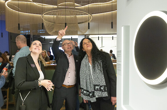 Gesprächssituation auf einem Messestand, Personen im Austausch unter ringförmiger Lichtinstallation und linearen Leuchten.