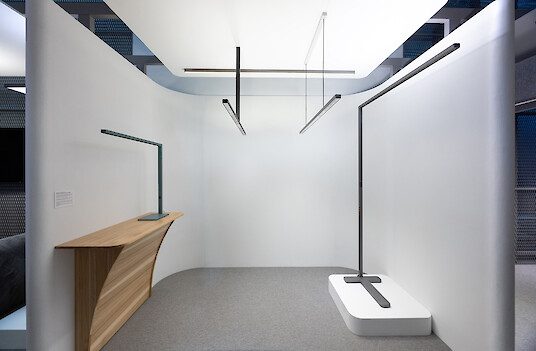 Minimalistischer Raum mit linearen Pendelleuchten, Arbeitsplatz und schlanken, freistehenden Leuchten auf Podesten