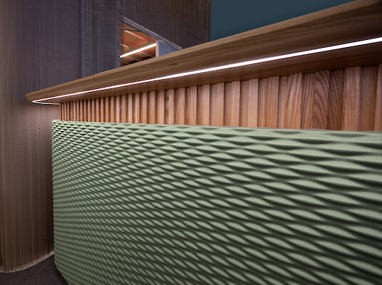 Holztheke mit integrierter Lichtlinie, strukturierte Oberfläche und textile Elemente auf Messestand