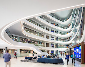A multi-story atrium with curved galleries, integrated lighting strips, and people in an open lounge area
