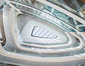 Curved atrium with surrounding light strips, a glass roof, and soft, flowing spatial forms